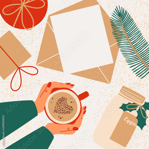 Human hands hold mug with coffee. Christmas gifts, fir branch, bottle with eggnog are scattered around the greeting card with copy space for text.