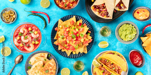 A panorama of Mexican food, many dishes of the cuisine of Mexico, flat lay, top shot on a blue background. Nachos, tequila, guacamole, quesadillas, shrimp cocktail, taco shells