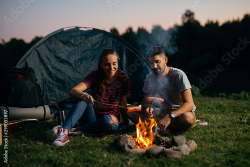 romantic couple on camping by the camping fire barbecuing sausages