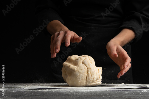 Pastry chef or baker cooks dough with flour, for sweets, rolls or Italian pizza or pasta. On a black background for design, for advertising or a signboard on a bakery, bakery banner