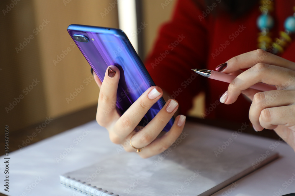 Fototapeta premium Girl makes notes in a notebook, uses a mobile phone wirelessly