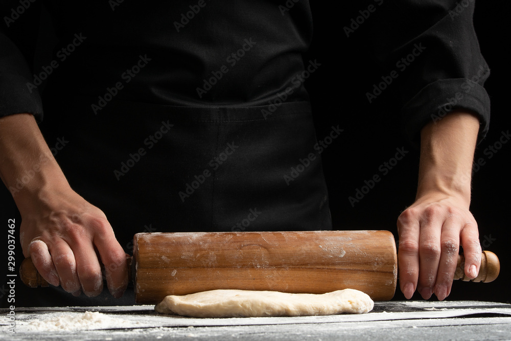 The chef cooks the dough under a rosquat press, for baking, bread, pizza, or pasta. on a black background The chef cooks the dough under a rosquat press, for baking, bread, pizza, or pasta. on a black background