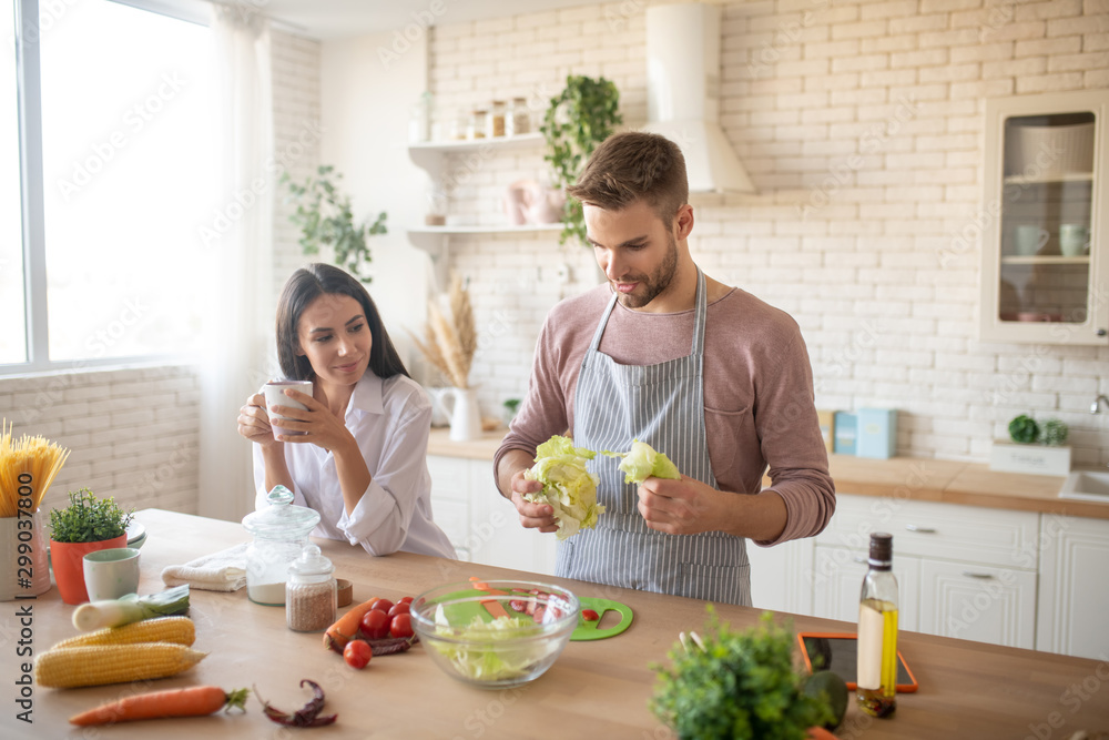 Bearded husband taking lettuce while cooking salad for wife