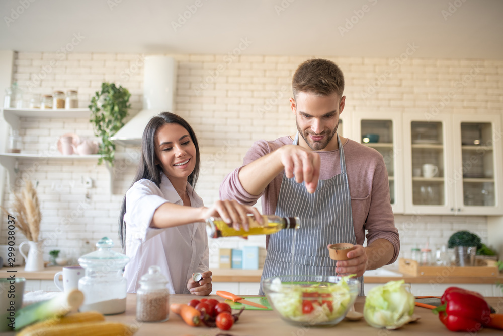 Husband adding spices to salad while cooking with wife