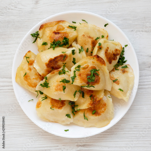 Homemade traditional polish fried potato pierogis on a white plate on a white wooden surface, top view. From above, flat lay, overhead. Closeup.