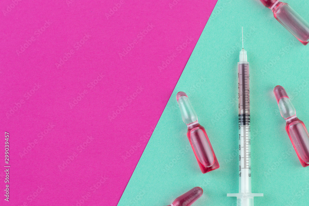 Ampoule and syringe with red liquid on colorful background. Flu vaccination. Catch-up immunization. Ampoule and syringe with red liquid on colorful background. Flu vaccination. Catch-up immunization.