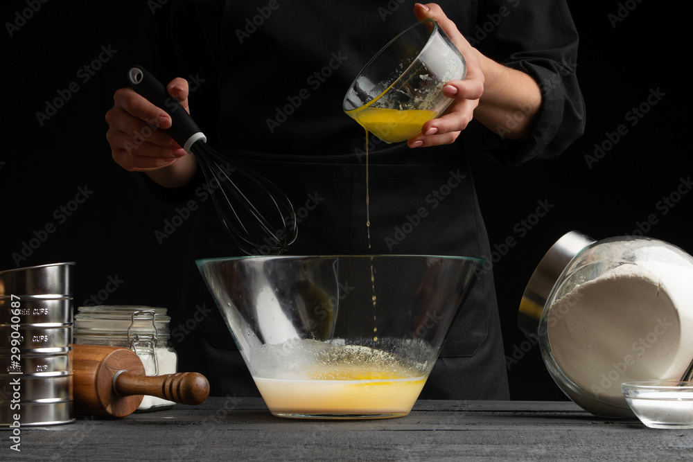 a pastry chef or baker cooks dough, pours yeast into a container, for making sweets, rolls or Italian pizza or pasta. Freezes in motion. On a black background, horizontal photo a pastry chef or baker cooks dough, pours yeast into a container, for making sweets, rolls or Italian pizza or pasta. Freezes in motion. On a black background, horizontal photo