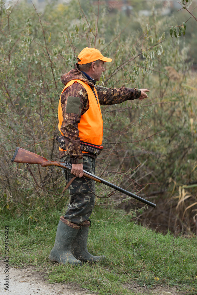 Hunting period, autumn season open. A hunter with a gun in his hands in hunting clothes in the autumn forest in search of a trophy. A man stands with weapons and hunting dogs tracking down the game. Hunting period, autumn season open. A hunter with a gun in his hands in hunting clothes in the autumn forest in search of a trophy. A man stands with weapons and hunting dogs tracking down the game.