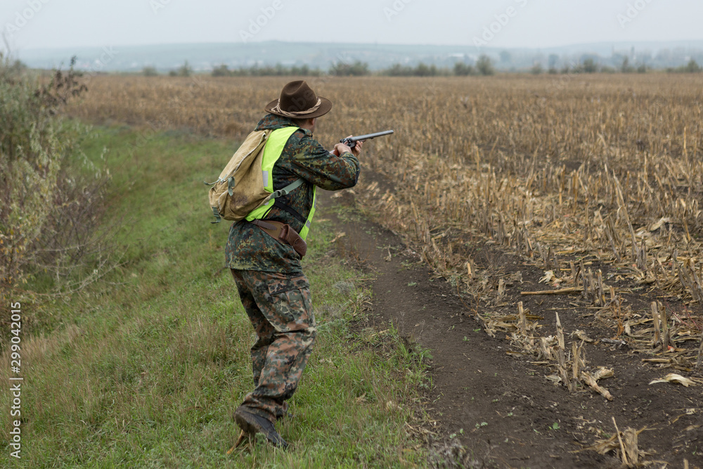 Hunting period, autumn season open. A hunter with a gun in his hands in hunting clothes in the autumn forest in search of a trophy. A man stands with weapons and hunting dogs tracking down the game. Hunting period, autumn season open. A hunter with a gun in his hands in hunting clothes in the autumn forest in search of a trophy. A man stands with weapons and hunting dogs tracking down the game.