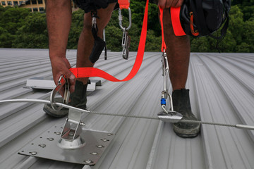 Male hand using transfer, clipping stainless industrial locking hook into the fall arrest roof anchor point systems, while tail is connected into his body personal safety harness in Sydney, Australia