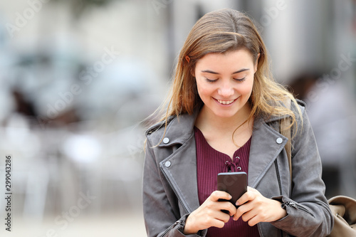 Happy girl texting on mobile phone in the street