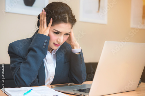 Stressed young businesswoman working in office with financial report on laptop