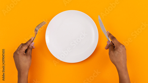 Fotografie, Obraz Black female hands holding empty plate on orange background, top view, free spac