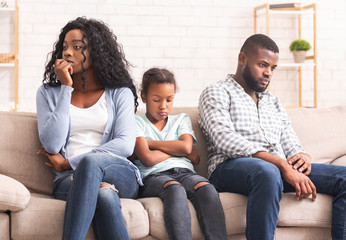Upset little girl suffer from family conflict, sitting between parents.