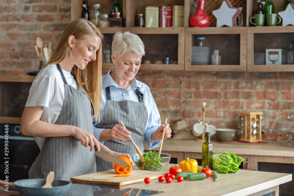 Young woman cooking healthy veggies salad with aged mom