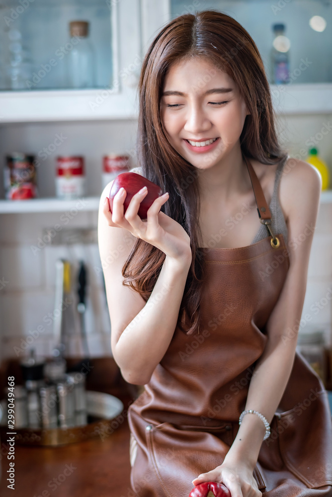 Young attractive Asian woman holding red apple on her hand at the kitchen in the morning Young attractive Asian woman holding red apple on her hand at the kitchen in the morning