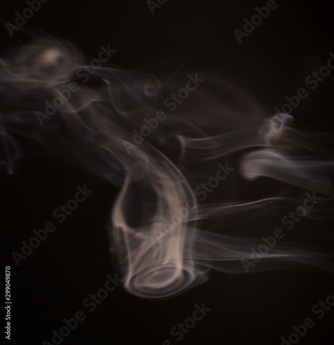 White steam spins and rises from the pan. White smoke rises from a large pot  which is located behind the frame. black background. Texture of smoky cloud