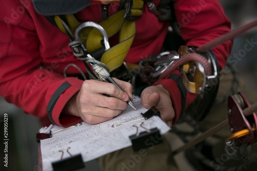 Close up picture of rope access technician engineer worker writing a report of building structure leak, hiatus at hight rise construction building site Sydney, city skyline, Australia      