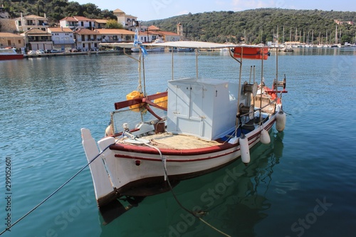 Old wooden fishing boat in calm blue sea water at the harbor of Vathy village in Meganisi island in Lefkada, Greece. Background view of the village yachts and sailing boats
