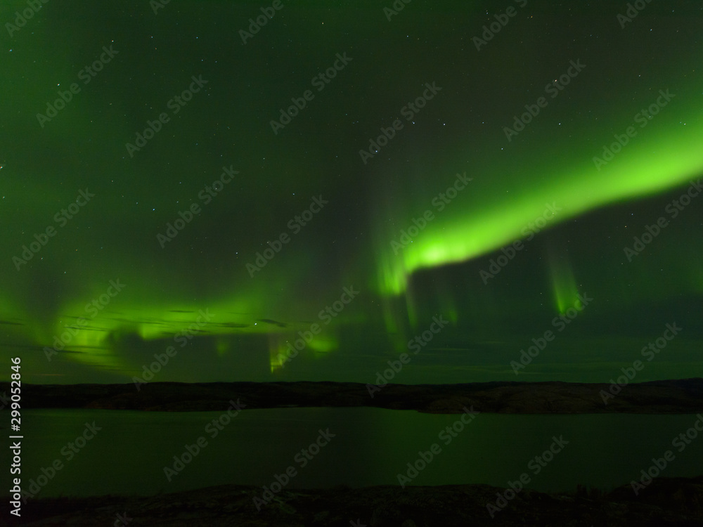 Northern lights over the lake and hills. Aurora at night in the sky in the north.
