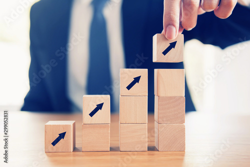 Business concept growth success process, Close up Businessman hand arranging wood cube with arrow stacking as step stair. photo