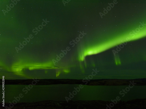 Northern lights over the lake and hills. Aurora at night in the sky in the north.