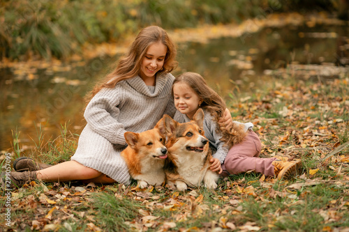 girls with two corgis sitting in the park at fall time