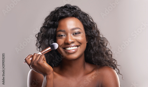 Фотография Beautiful african woman applying blush on face with brush tool