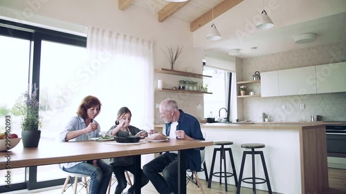 A small girl with senior grandparents indoors sitting at the table, eating. photo