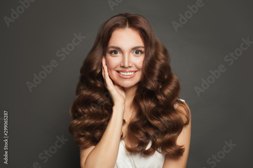Cute young woman with long healthy brown curly hair smiling. Pretty female model portrait