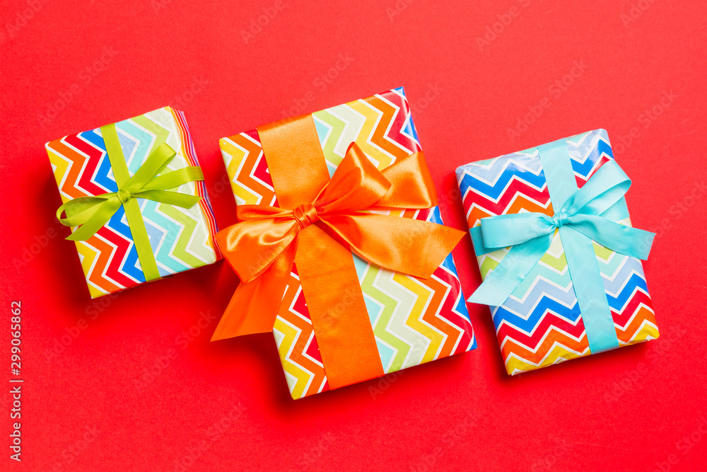 wrapped Christmas or other holiday handmade present in paper with blue, green and orange ribbon on red background. Present box, decoration of gift on colored table, top view wrapped Christmas or other holiday handmade present in paper with blue, green and orange ribbon on red background. Present box, decoration of gift on colored table, top view