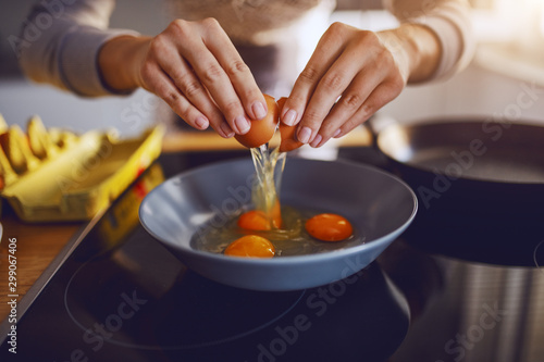 Close up of caucasian woman breaking egg and making sunny side up eggs. Domestic kitchen interior. Breakfast preparation.