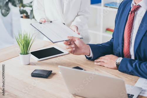 cropped view of businesswoman holding clipboard near businessman sitting at workplace