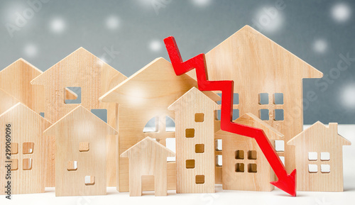 Miniature wooden houses and down arrow. The concept of low housing demand. Discounts for real estate in the winter. Mortgage, loan. Cheap cost. Christmas Snowflakes