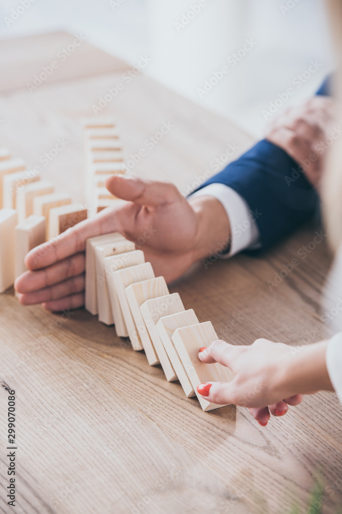 cropped view of woman pushing wooden block and risk manager blocking domino effect cropped view of woman pushing wooden block and risk manager blocking domino effect