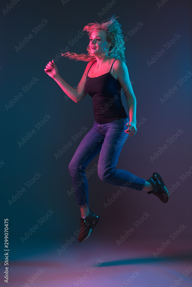 Caucasian young woman's portrait on gradient background in neon light. Beautiful female model with unusual look. Concept of human emotions, facial expression, sales, ad. Jumping, smiling.