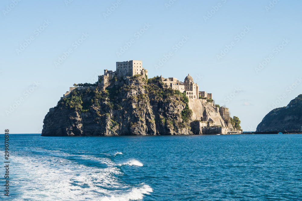 View from sea on Aragonese castle surrounded by sea, town a port with boats on Ischia island in Italy