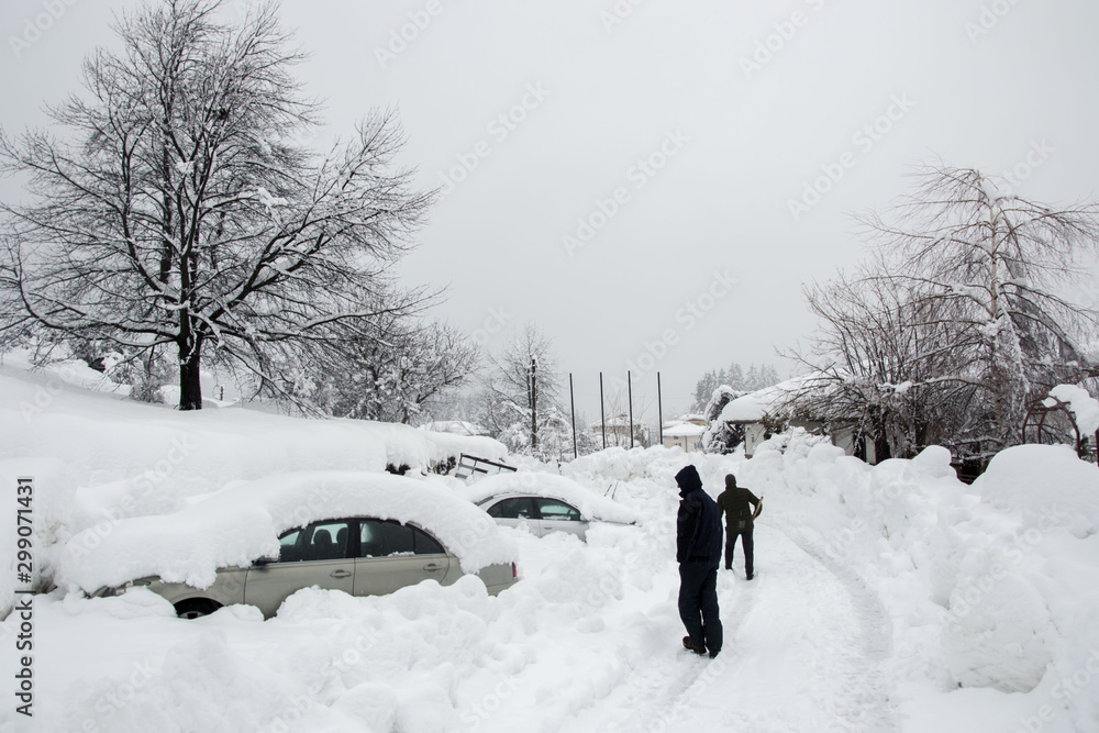 Unrecognizable man cleaning the snow in front of a car, covered in snow. People and vehicle concept. Cleaning snow, snowfall during winter season Unrecognizable man cleaning the snow in front of a car, covered in snow. People and vehicle concept. Cleaning snow, snowfall during winter season