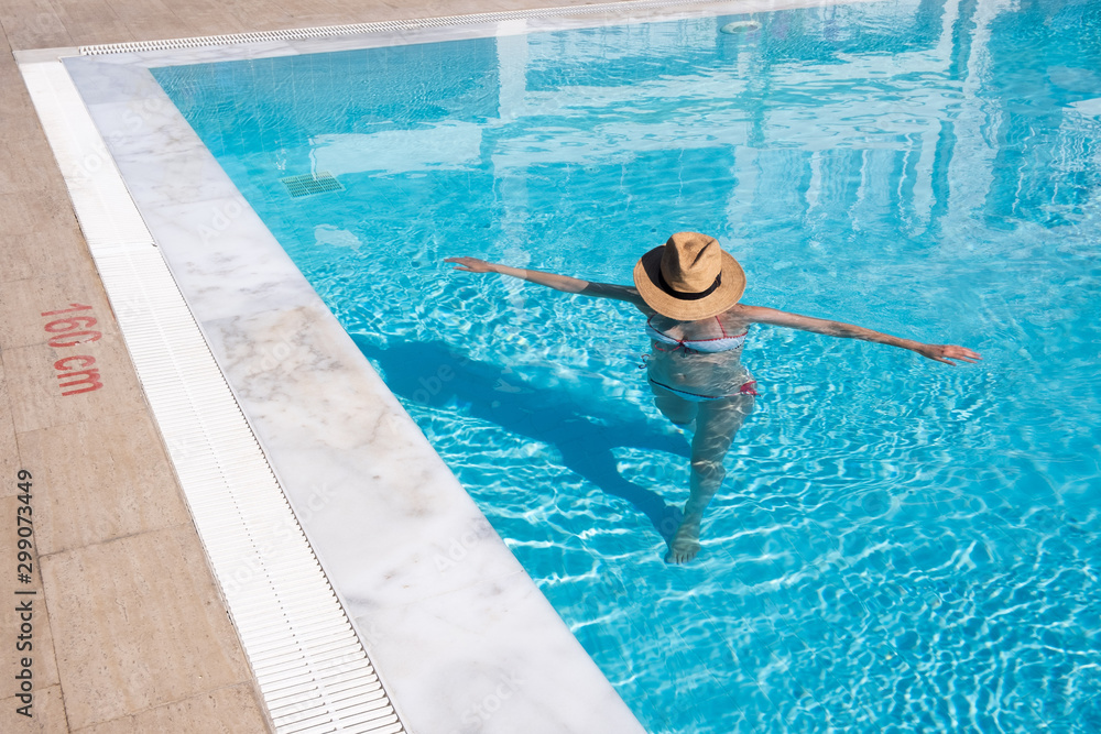 woman walking in a swimming pool with hat covering her face
