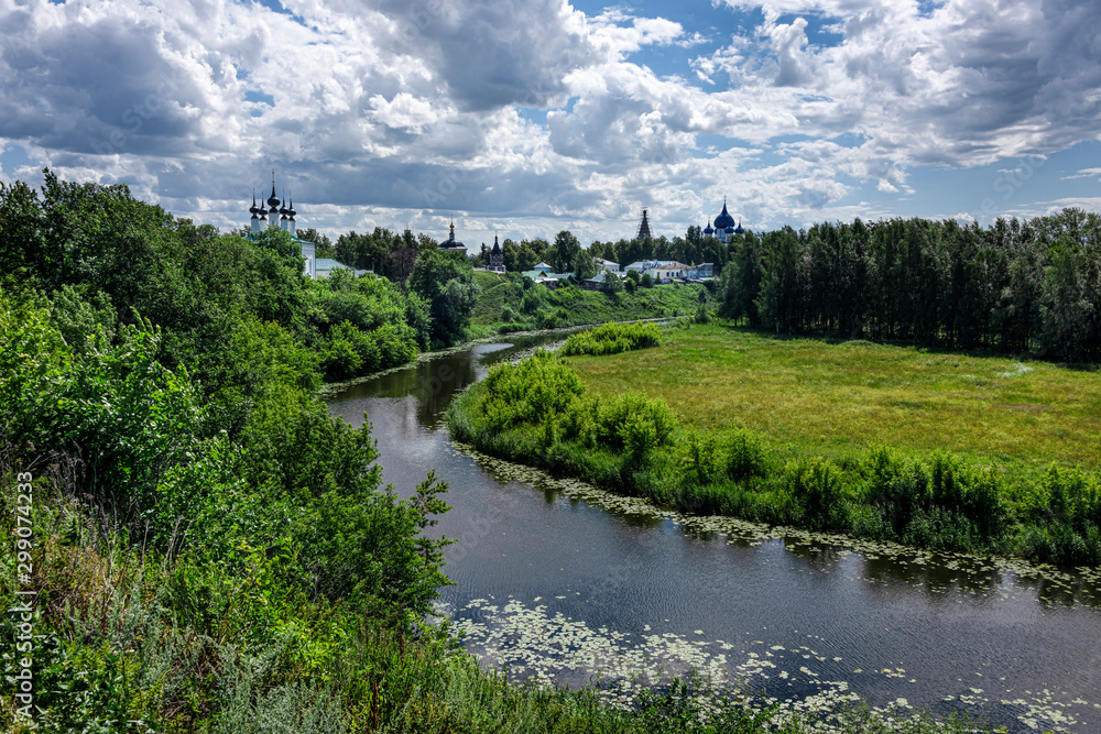 Fototapeta premium Russia, Vladimir Oblast, Golden Ring, Suzdal: Panorama view with river Kamenka, green riverside and famous old orthodox churches, monasteries, convents in one of the oldest Russian towns, blue sky.