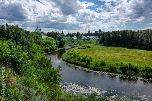 Russia, Vladimir Oblast, Golden Ring, Suzdal: Panorama view with river Kamenka, green riverside and famous old orthodox churches, monasteries, convents in one of the oldest Russian towns, blue sky.