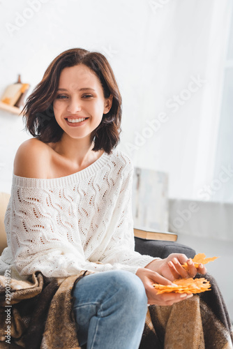 beautiful happy brunette girl holding yellow autumn leaves at home