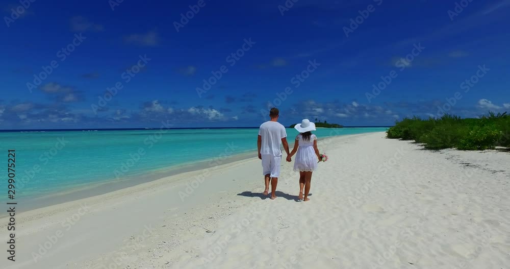 Couple on white dresses walking on tropical beach along coastline, girl hold on her hand a bouquet with roses, Thailand Couple on white dresses walking on tropical beach along coastline, girl hold on her hand a bouquet with roses, Thailand