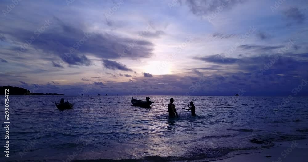 Light purple sky after sunset on background of a happy couple playing with warm water on island's bay with fishing boats, Philippines Light purple sky after sunset on background of a happy couple playing with warm water on island's bay with fishing boats, Philippines