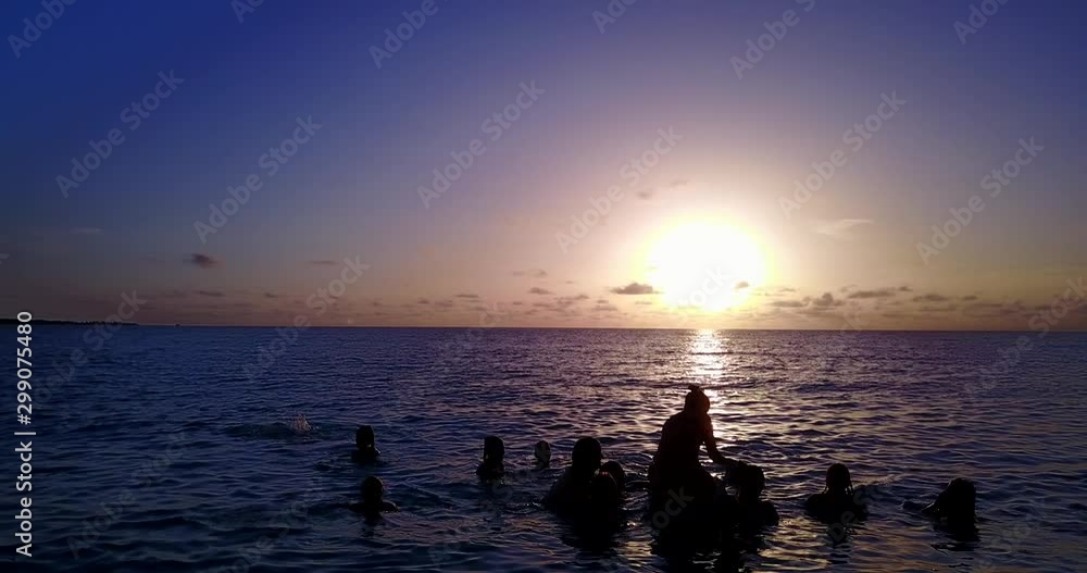 Large group of young people in vacation playing in warm seawater at magical sunset with violet to orange color specter in The Maldives Large group of young people in vacation playing in warm seawater at magical sunset with violet to orange color specter in The Maldives