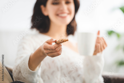 selective focus of happy girl with cup of coffee holding cookie