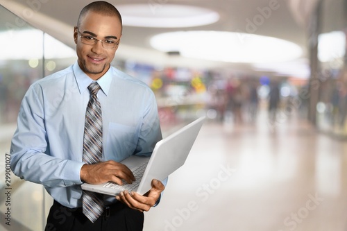 Smiling African Student man with laptop, mall background, bokeh © BillionPhotos.com