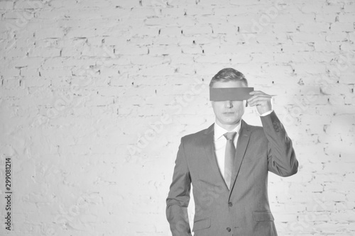 Mature businessman covering eyes with paper against white brick wall at office