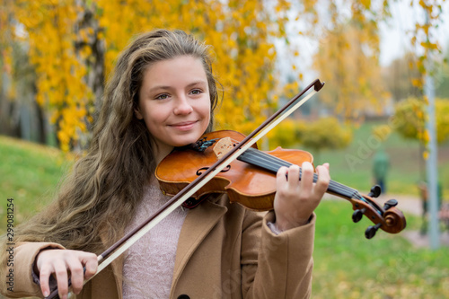 Obraz na płótnie Girl playing the violin in the autumn park at a yellow foliage background. w salonie
