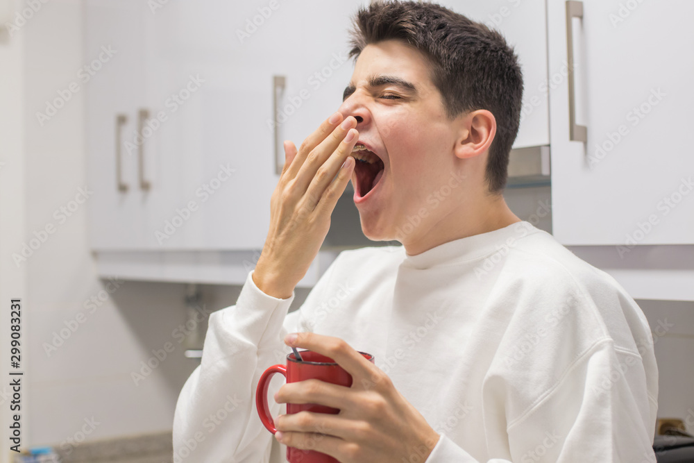young man at home with cup of coffee yawning young man at home with cup of coffee yawning